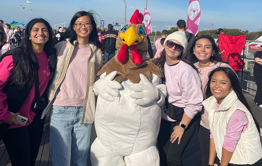 Nursing students posing with a turkey mascot at a breast cancer awareness event. 