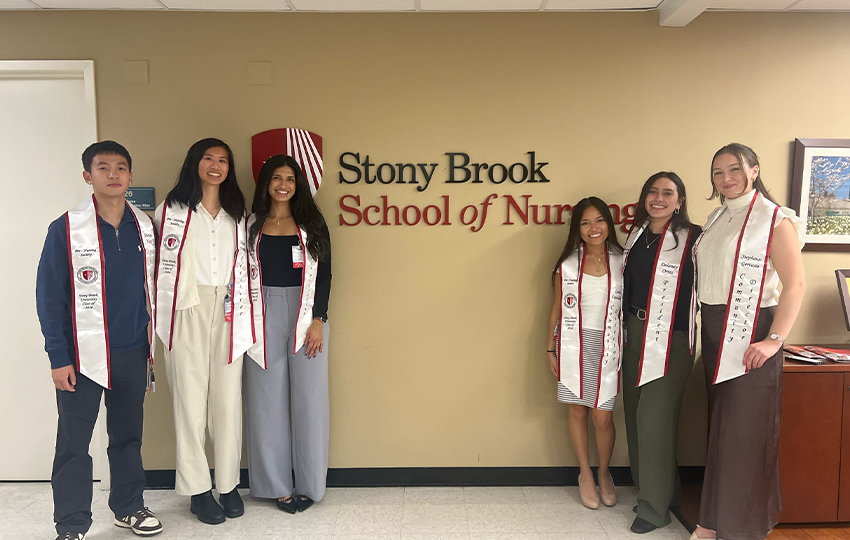 Nursing students posing in front of a Stony Brook School of Nursing sign. 